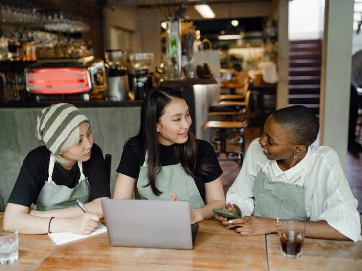 Illustrative photo: café staff in aprons planning at a table with a laptop